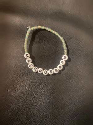 Pärlarmband med text Maskrosbarn - Unikt armband med små gröna och vita pärlor samt vita bokstavspärlor som bildar ordet 'MASKROSBARN'. Perfekt för dig som vill ha ett personligt smycke med betydelse. Armbandet är elastiskt och passar de flesta handleder.
