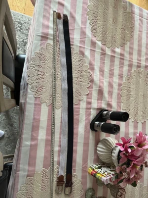 Två flätade bälten i svart och vitt - Säljer två snygga flätade bälten, ett i svart och ett i beige. Båda har detaljer i brunt skinn vid ändarna och klassisk metallspänne. Perfekta för att lyfta vilken outfit som helst och passar till både jeans och byxor.