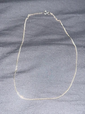 Tunt silverfärgat kedjehalsband - Snyggt och enkelt halsband i silverfärg med tunn, fyrkantig kedja. Perfekt för dig som gillar minimalistisk stil och vill ha ett smycke som funkar till många olika looks. Halsbandet har ingen synlig logga eller  märke och är gjort i metall. 43cm lång. Frågor? Skriv gärna