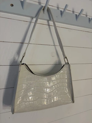 Vit axelremsväska  - Vit handväska från SHEIN. Den har inga fickor i sig, och är lite sliten vilket jag visat i bilderna. Men utöver det är den i väldigt fint skick. Hör gärna av dig om du undrar över något!