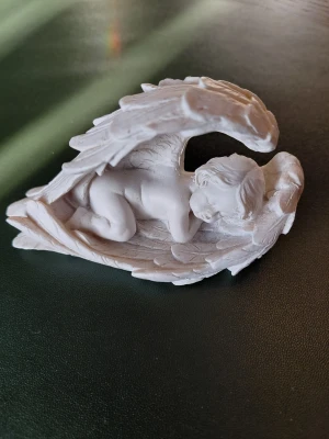 Vit ängel-bebis prydnadsfigur - Nästan ny Dekorativ prydnadsfigur i vitt som föreställer en sovande bebis inbäddad i stora änglavingar. Figuren är detaljerad med fjäderstruktur på vingarna. Tillverkad i keramik eller liknande material, perfekt som dekoration eller present.