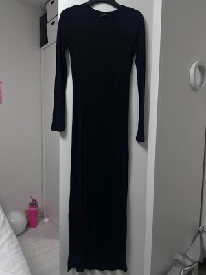 Svart långärmad maxiklänning - ginatricot - En svart, långärmad maxiklänning med rund halsringning. Klänningen har en smal passform och är tillverkad i ett mjukt, stretchigt material som ger en snygg siluett. Perfekt för dig som gillar en enkel och stilren look.