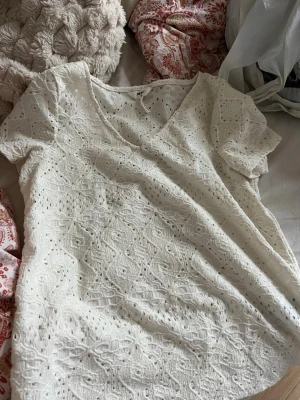 Vit spetsblus med v-ringning Object - Söt vit blus från Object i storlek XS. Blusen har v-ringning, korta ärmar och är täckt av ett broderat spetsmönster som ger en romantisk vibe. Perfekt till jeans eller kjol för en fräsch look.
