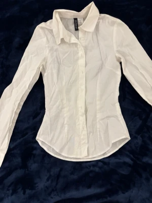 Vit tight skjorta från H&M Divided - Klassisk vit skjorta från H&M Divided med lång ärm och knappar framtill. Använd en gång vid halloween men väldigt snygg och passar fint.