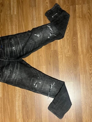 Svarta jeans från Jack & Jones  - Säljer ett par svarta jeans från Jack&jones med en väldigt skön look då den har slitningar och lite färgstänk på! Dessa byxor passar bra om man vill ha lite unik stil eller klä sig mer i grisch/orten stilen. Passar även med andra stilar. HELT oanvända men saknar lapparna