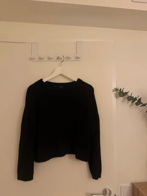 Svart stickad tröja - En enkel och stilren svart stickad tröja med rund hals och långa ärmar. Tröjan har en något kortare passform och är perfekt att matcha med jeans eller kjol. Materialet är mjukt och bekvämt, vilket gör den skön att bära under kyliga dagar.