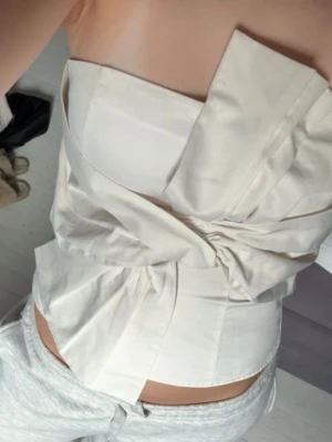 Vit bandoutopp  - Trendig beige tubtopp med omlottdetalj och stor knut framtill. Använd en gång, köpte på Plick men är från hm! 