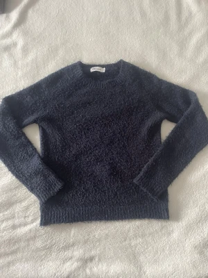 Mörkblå fluffig stickad tröja - Mysig mörkblå stickad tröja från D6 Soul med fluffig textur. Tröjan har rund halsringning, långa ärmar och ribbstickade muddar.