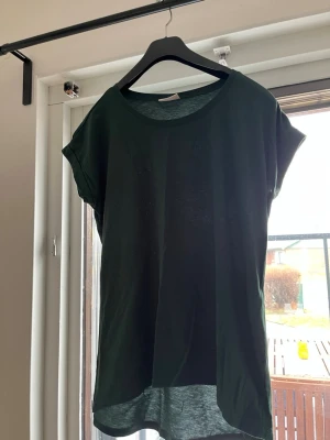 Mörkgrön t-shirt från Vila - En stilren mörkgrön t-shirt från Vila med rund halsringning och korta ärmar. T-shirten har en något längre bakdel och är tillverkad i mjuk bomull, perfekt för en avslappnad look.