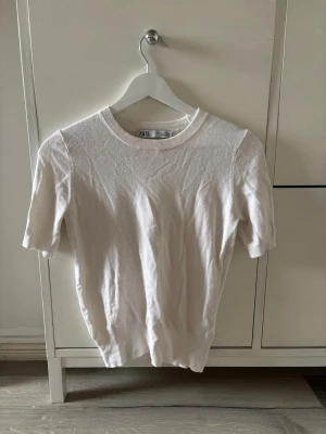 Vit kortärmad topp från Zara - En enkel och stilren vit topp från Zara med rund halsringning och korta ärmar. Tillverkad i mjukt bomullsmaterial som känns skönt mot huden. Perfekt att matcha med jeans eller kjol för en clean look.💕