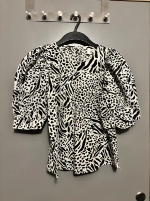 Svartvit leopard & zebra puffärmsblus från H&M - Trendig blus från H&M med svartvitt djurmönster och stora puffärmar. Blusen har rund halsringning och är tillverkad i ett lätt tyg som ger en snygg siluett. Perfekt för dig som vill sticka ut med ett coolt mönster och voluminösa ärmar.
