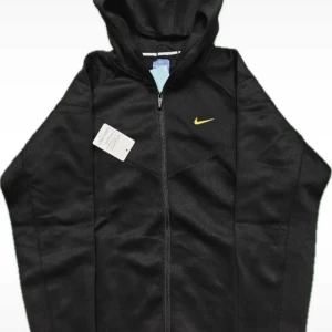 Svart Nike hoodie - Snygg svart hoodie från Nike med dragkedja framtill och gul Nike-logga på bröstet. Huva med snörning och diskreta detaljer i gult på ärmen och ryggen. Tillverkad i mjukt material som passar perfekt till en avslappnad stil.