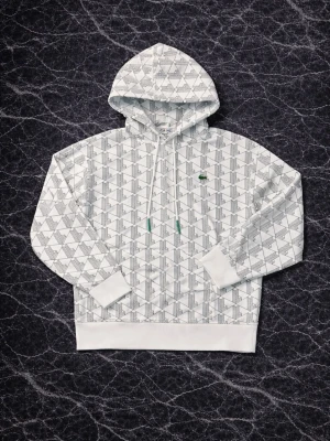 Vit Lacoste hoodie - Snygg vit hoodie från Lacoste med svart grafiskt mönster över hela plagget och klassisk krokodillogga på bröstet. Storlek S men passar också lite större. Priset är diskuterbart🙌