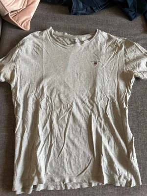 Ljusgrå t-shirt från GANT - Ljusgrå t-shirt från GANT med klassisk rund hals och korta ärmar. Diskret logotyp på bröstet. Tillverkad i mjuk bomull som är skön att bära. Perfekt för dig som gillar stilrena basics.