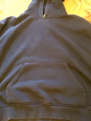 Mörkblå hoodie med magficka - En enkel och stilren mörkblå hoodie med klassisk huva och stor magficka framtill. Hoodien har ribbade muddar vid ärmslut och nederkant. Perfekt för en avslappnad och bekväm look. Materialet känns mjukt och skönt mot huden.