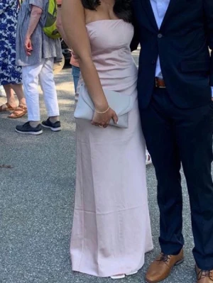 Ljusrosa satin balklänning  - Elegant ljusrosa långklänning i satinliknande material. Klänningen är axelbandslös med öppen rygg och dekorativa knappar bak samt korsade band. Perfekt för student eller sommarens festligheter. Endast använd en gång. Storlek S 🥰