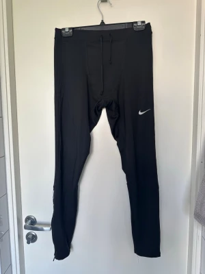 Herr- Svarta träningstights från Nike M - Säljer ett par svarta träningstights från Nike med dragsko i midjan och klassisk vit Nike-logga på benet. Tillverkade i stretchigt funktionsmaterial som passar perfekt för löpning eller gym. Tight passform och långa ben.