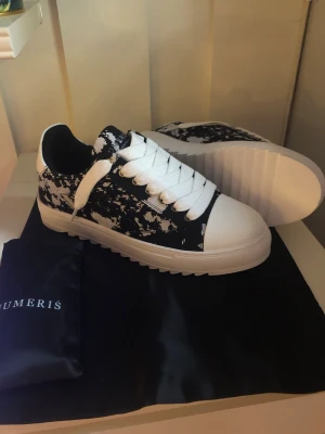 Svartvita sneakers från Numeris - Snygga sneakers från Numeris i svart och vitt med coolt splattermönster. Skorna har breda vita skosnören, vit tå och tjock vit sula med räfflad kant. Perfekta för dig som vill sticka ut med din stil.