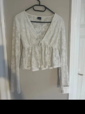 Vit spetsblus med knytning - Söt vit blus från Gina tricot i väldigt fint mönster. Djup v-ringning och knytning framtill, samt volang nedtill för en romantisk look. Långa ärmar som är lite bredare och toppen är väldigt luftig och skön att ha nu i sommar till exempel. Den är också nästan aldrig använd. 