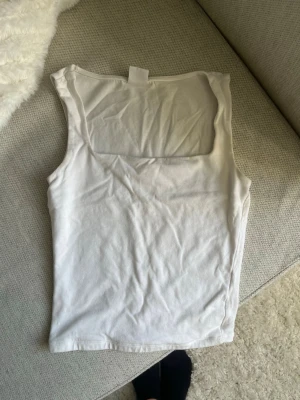 Vit linnetopp från Gina Tricot - Säljer en enkel och stilren vit linnetopp från Gina Tricot, kollektionen Elevated Basics. Toppen är ärmlös med rund halsringning och tillverkad i mjuk bomull. Perfekt att matcha med jeans eller kjol för en clean look.