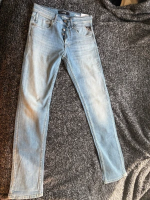 Ljusblå slim fit Replay jeans  - Säljer ett par ljusblå slim fit  jeans från Replay med klassisk femficksmodell och knappgylf. Jeansen har en smal passform och är tillverkade i mjukt denimtyg. Perfekta för en avslappnad och trendig look.