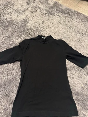 Svart polotopp från Lindex - En svart polotopp från Lindex i mjuk bomull. Toppen har halvlånga ärmar och en högre krage som ger en clean och stilren look. Perfekt att matcha med jeans eller kjol för en enkel men snygg outfit.