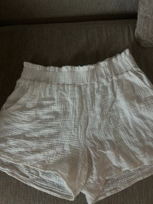 Vita luftiga shorts i bomull - Säljer ett par vita, löst sittande shorts i mjuk och krinklad bomull. De har hög midja med resår och praktiska sidofickor. Perfekta för varma sommardagar och riktigt sköna att bära. De är i 42 men dessa sitter skönt/snyggt på mig som vanligtvis är 36-38