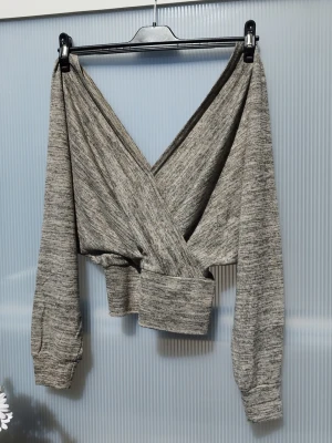 Grå/Beige omlottopp med lång ärm - Snygg grå/beige omlottopp med lång ärm och bred mudd i midjan. Toppen har en croppad passform och är tillverkad i mjukt material som känns skönt mot huden. Perfekt för dig som gillar en avslappnad men trendig stil. Köpt på Nelly, storlek Eu 44. Använd någon enstaka gång. 