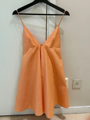  Ny trendig orange klänning från Zara  - Säljer ett persikofärgat klänning med tunna axelband och v-ringning. Klänning har en lös och luftig passform, perfekt för varma nätter. Materialet ser ut att vara mjukt och bekvämt, troligen bomull e. Enkel och stilren design.