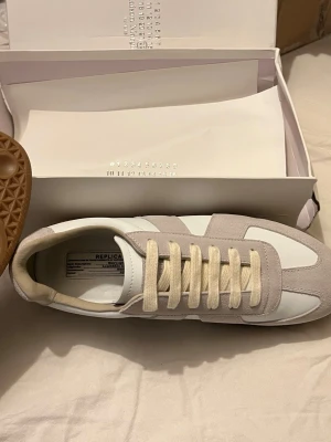 Maison Margiela  - Maison Margiela sneakers i beige mocka och vitt läder med klassisk gummisula. Snygg retrostil med beige snörning och diskreta detaljer. Perfekt för dig som gillar minimalistisk och stilren design.