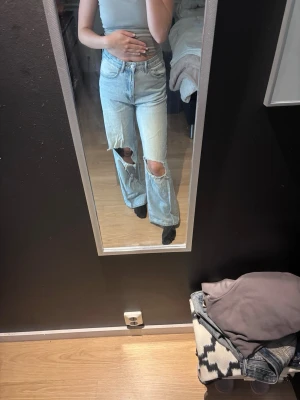 Ljusblå ripped straight leg jeans - Säljer ett par ljusblå jeans med raka ben och stora slitningar över knäna. Jeansen har hög midja och klassisk femficksmodell. Perfekta för en avslappnad och trendig look. Materialet är denim i bomull.