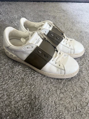 Valentino open olivgrön - Snygga vita sneakers från Valentino med bred grå läderdetalj över snörningen. Klassisk låg modell med rund tå och vita skosnören. Märkeslogga på plösen och stilren design som passar till det mesta. Tillverkade i läder för en exklusiv känsla. Storlek 42