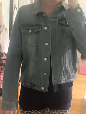Grön jeansjacka från LAB Industries - Snygg grön jeansjacka från LAB Industries med klassisk krage, två bröstfickor med lock och silverfärgade knappar. Jackan är i denim och har en rak passform som passar perfekt till många olika stilar.