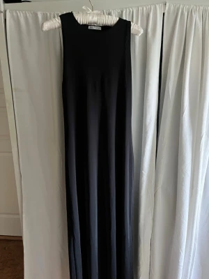 Svart långklänning från Zara - En stilren svart långklänning från Zara med ärmlös design och rund halsringning. Klänningen har en rak och enkel siluett som ger en clean look. Använd en gång.