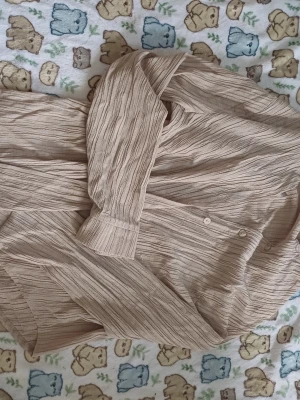 Beige strukturerad blus med knappar - Säljer en beige blus med lång ärm och diskret strukturmönster i tyget. Blusen har knäppning framtill och en avslappnad passform. Materialet känns lätt och luftigt, perfekt för en stilren look. Lite lätt skav av trådar på sidan 