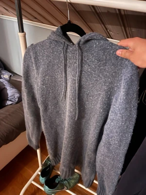 Merinoull hoodie från dressmann - Mysig hoodie i melerad blå färg med huva och dragsnören. Tillverkad i ett mjukt, stickat material som känns riktigt skönt mot huden. Långa ärmar och ribbade muddar vid ärmslut och nederkant. Perfekt för dig som gillar en avslappnad och stilren look.