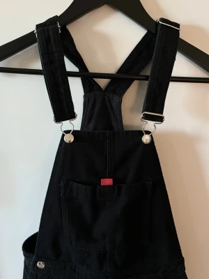 Svart Adidas jumpsuit med hängslen - hängselbyxa från Adidas. Tillverkade i ett slitstarkt men även stretchigt bomullstyg. Endast använd några gånger 