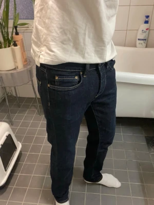 Mörkblå denim jeans - Säljer ett par mörkblå jeans med raka ben och klassisk femficksmodell. Jeansen har kontrastsömmar och metallnitar vid fickorna. Passar perfekt till en avslappnad stil och är tillverkade i ett robust denimtyg.