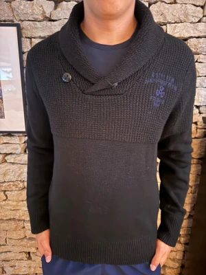 G star - Mörk stickad tröja från g star med sjalkrage och knappdetalj. Tröjan har broderad logga på bröstet och är ribbstickad upptill samt vid muddar och nederkant. Perfekt för dig som gillar en stilren och modern look.