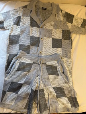 Gråmelerat stickat set  - Sommaren är här och nu har jag nyss set med kortärmad skjorta och shorts. Setet har ett rutigt mönster i olika nyanser av grått och vitt, knappar framtill och dragsko i midjan på shortsen. Materialet är luftigt och mjukt, perfekt för en avslappnad look. Du får gratis glasögon på köpet