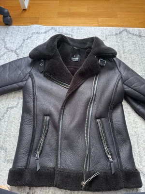 Svart pälsjacka från Stradivarius - Säljer en svart pälsjacka från Stradivarius med bred krage, asymmetrisk dragkedja och två snedställda fickor med dragkedjor. Jackan har mjukt foder i fuskpäls och detaljer i läderimitation. Perfekt för kalla vinterdagar. Hål i fickorna men det går att sy det är värt det, storlek Xs men passar upp till L