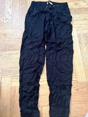 Svarta mjukisbyxor från H&M - Svarta mjukisbyxor från H&M med resår och dragsko i midjan. Byxorna har smal passform och muddar vid bensluten. Perfekta för en avslappnad stil och tillverkade i mjukt material som känns skönt mot huden.