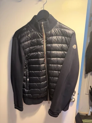 Svart dunväst från Moncler - Snygg svart MALIGA Cardian  från Moncler med quiltad framsida och mjuka ärmar i sweatshirtmaterial. Dragkedja framtill med Monclers signaturband och logga på ärmen. Perfekt för lager-på-lager och streetwear-vibe. Hej Säljer min Moncler MALIGA som är knappt Använd Köptes på Kaspersheat.com För då 4000+ Nypris Mellan 10000/10500  Priset är Både Prutat och klart och Fast Pris kan skickas om du Står För Frakten Köparskyddet     har du Frågor Fråga Gärna Tack!😊