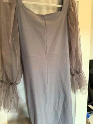 Ljusgrå klänning med puffärmar - Trendig ljusgrå klänning med transparenta puffärmar i mesh och rynkade detaljer framtill. Klänningen har en fyrkantig ringning och är figurnära med snygg drapering. Perfekt för dig som vill sticka ut med en unik och elegant look.