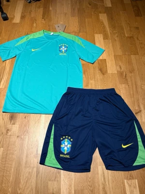 Brazil summer set turkos  - Snyggt träningsset från Nike med Brasil-logga. T-shirten är turkos med ljusgröna axelpartier och gul Nike-logga. Shortsen är mörkblå med gröna detaljer och har både Nike-logga och Brasil-märke. Perfekt för fotbollsträning eller gymmet.