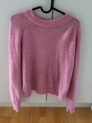 Rosa stickad tröja med rund hals - Mysig rosa stickad tröja med rund halsringning och långa ärmar. Tröjan har ribbstickade muddar vid ärmslut och nederkant. Perfekt för kyliga dagar och enkel att matcha med olika outfits.