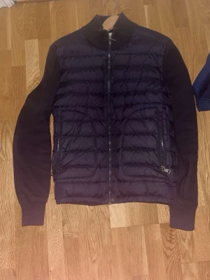 Mörkblå cardigan från Moncler - Snygg cardigan från Moncler med quiltad front och släta ärmar. Jackan har hög krage, två dragkedjeförsedda fickor och hel dragkedja framtill. stilren look.