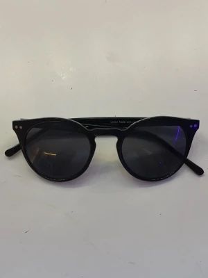 Svarta solglasögon - Snygga svarta solglasögon med rundad form och mörka glas. Klassisk design som passar till de flesta outfits. Bågarna är i blank plast och har små silvriga detaljer vid hörnen. Perfekta för soliga dagar. Från lindex.