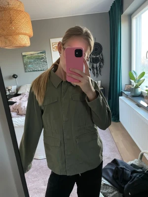 Olivgrön vårjacka  - Snygg olivgrön overshirt med fyra stora fickor framtill och klassisk krage. Jackan är tillverkad i bomull och har en rak passform med långa ärmar. Perfekt att slänga över en hoodie eller t-shirt för en chill look.