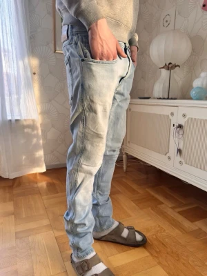 Ljusblå Replay ANBASS - Säljer ett par ljusblå jeans från Replay med skön passform och klassiska fem fickor. Jeansen har en avslappnad vibe och är tillverkade i mjuk denim. Snygga slitningar och detaljer på bakfickorna ger extra stilpoäng.